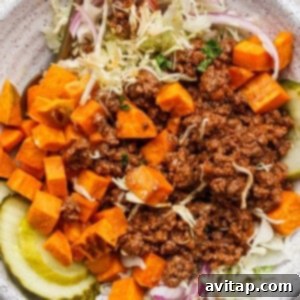 A fully assembled Sloppy Joe Bowl, featuring ground beef, diced sweet potatoes, sliced pickles, shredded lettuce, and red onion slices, ready to be enjoyed with a fork resting beside it.