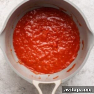 A beige pan filled with rich red tomato sauce on a gray textured surface, showing the sauce preparation for sloppy joes.