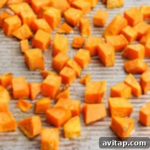 Uniformly chopped sweet potato pieces are spread out in a single layer on a baking tray, ready for roasting.