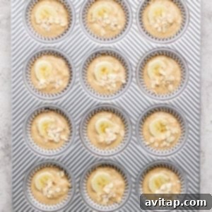 A muffin tray with twelve muffin batter portions, each beautifully topped with banana slices and a sprinkle of oats, perfectly arranged and ready for baking in the oven.