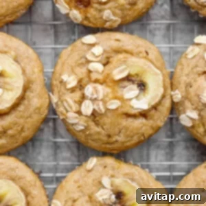 Warm banana oat muffins resting on a cooling rack, each topped with a thin banana slice and oats, awaiting to be enjoyed as a wholesome treat.