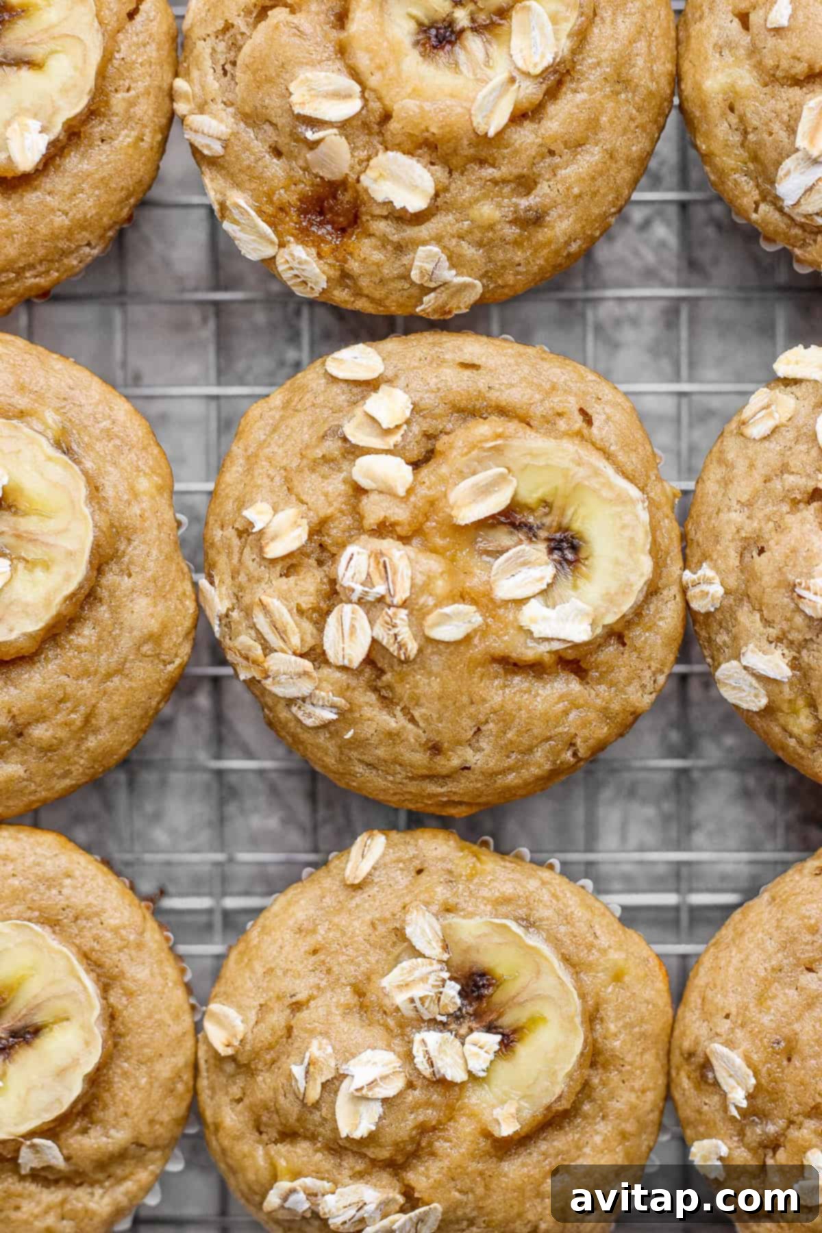 Freshly baked banana oat muffins, garnished with banana slices and a sprinkle of oats, arranged neatly on a wire cooling rack against a light background.