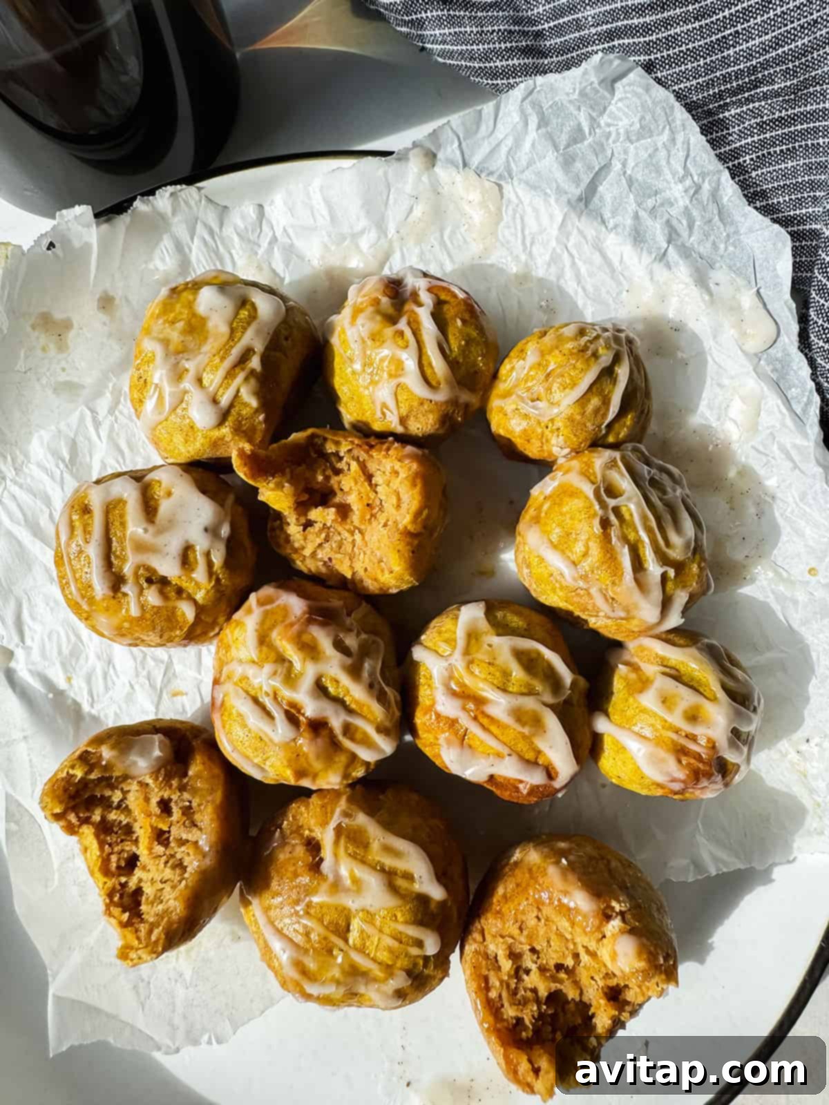 A plate of small, round pumpkin bagel bites drizzled with white icing, some partially eaten, on a piece of parchment paper, highlighting their delicious texture and glaze.