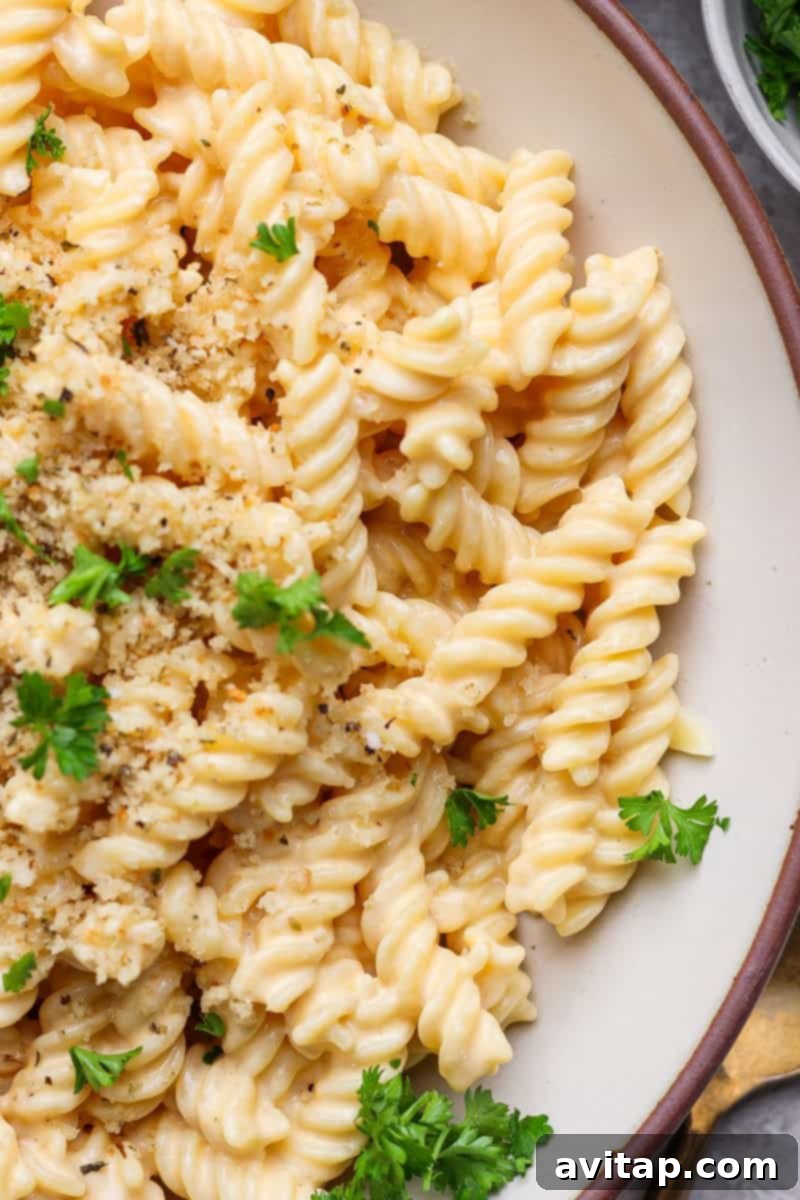 A close-up of a bowl of creamy pasta topped with golden breadcrumbs and garnished with fresh parsley, highlighting its rich texture.