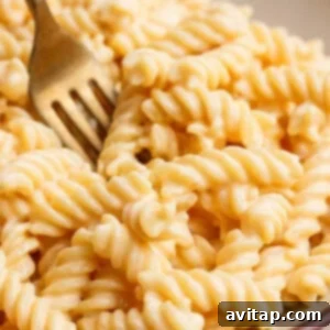 Close-up of a fork in a bowl of creamy, spiral macaroni and cheese.