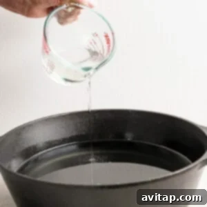 Hand pouring liquid from a measuring cup into a black cast iron pan.
