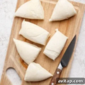 Six pieces of dough are placed on a wooden cutting board next to a knife.
