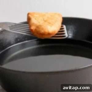 A golden-brown hash brown on a spatula over a black frying pan.