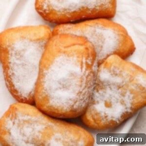 A plate of six sugar-dusted beignets on a white dish.