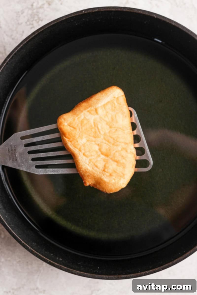 Nonna Marie's Crispy Fried Pizza 5 A piece of fried bread being lifted from a pan of oil with a metal spatula.