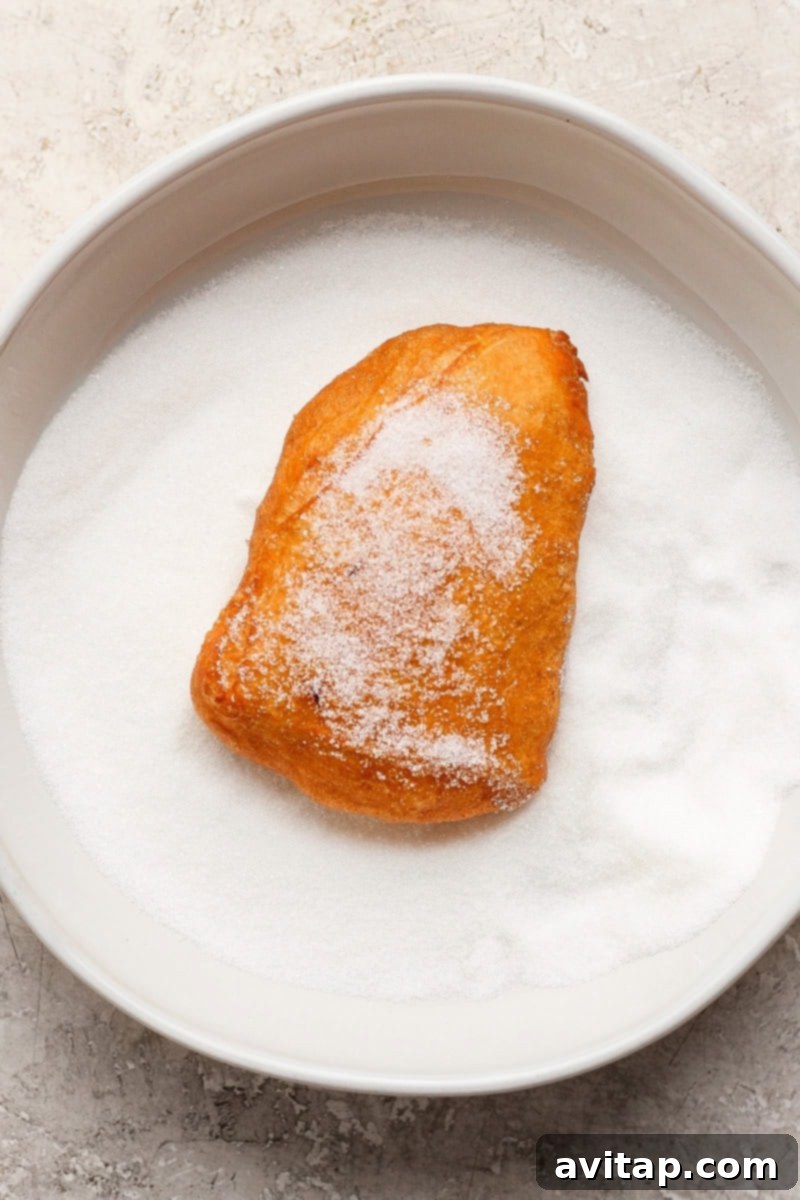 Nonna Marie's Crispy Fried Pizza 7 A sugar-covered pastry sits on a plate filled with granulated sugar.