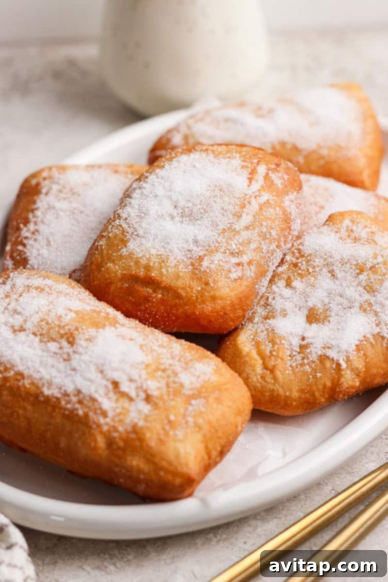Nonna Marie's Crispy Fried Pizza 8 A plate of rectangular beignets coated with powdered sugar on a light-colored surface.
