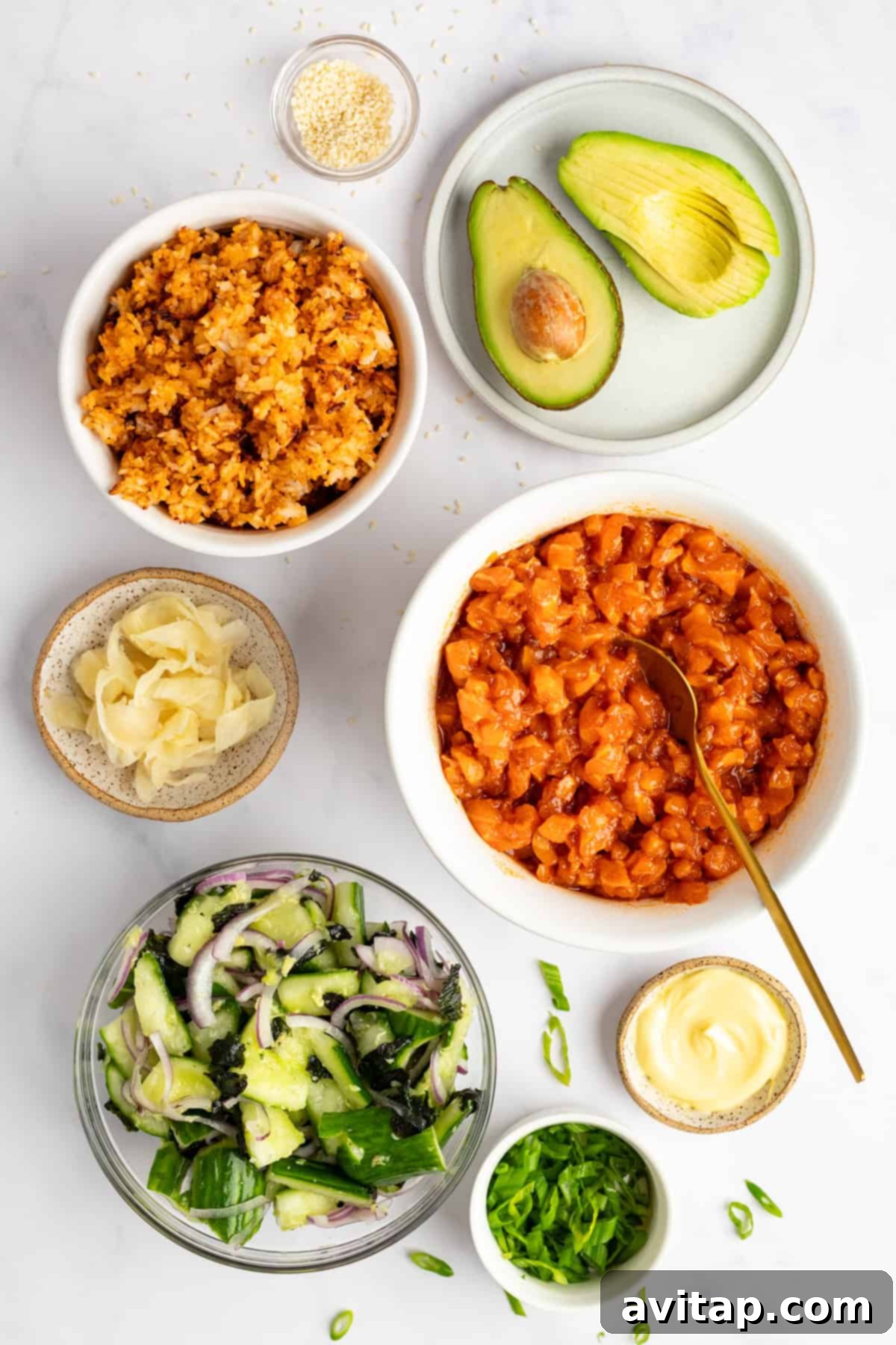 Ingredients for poke bowl on a white surface: raw salmon, sliced avocado, rice, cucumber salad, pickled ginger, sliced onions, mayonnaise, sesame seeds, and chopped green onions.