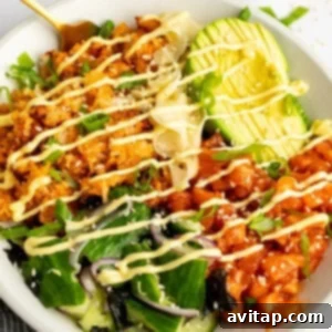 A bowl with rice, avocado slices, diced fish, greens, and seaweed, topped with mayonnaise drizzle and sprinkled with sesame seeds and green onions.