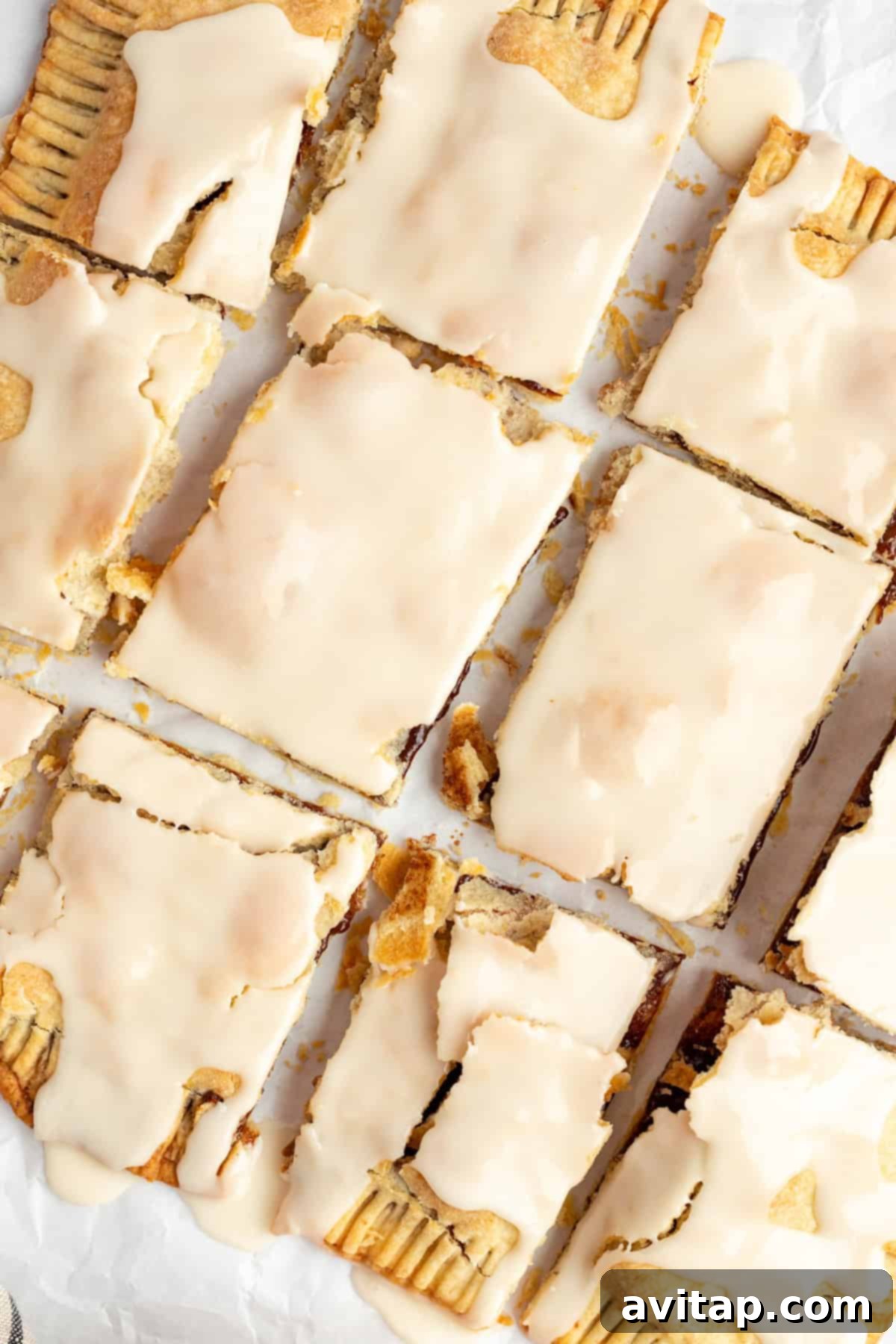 Fit Frosted Pastries 2 Rectangular pastries covered with a light beige icing are arranged in a 3x4 grid on a sheet of parchment paper, showcasing the delicious homemade Protein Pop Tarts ready to be served.