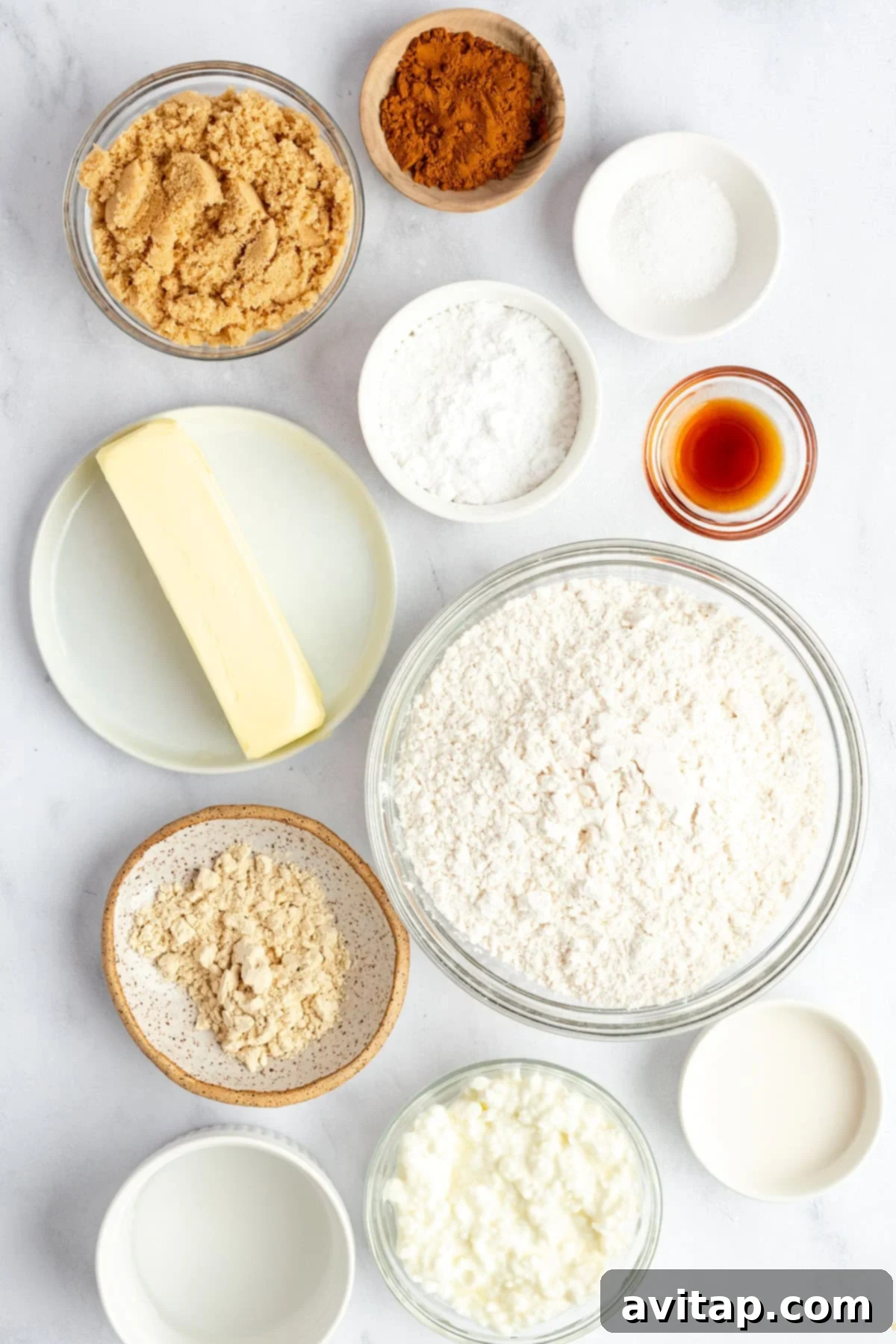 Fit Frosted Pastries 4 Assorted baking ingredients, including flour, brown sugar, butter, and cinnamon, neatly arranged in bowls and plates on a white surface, ready for preparing homemade treats.