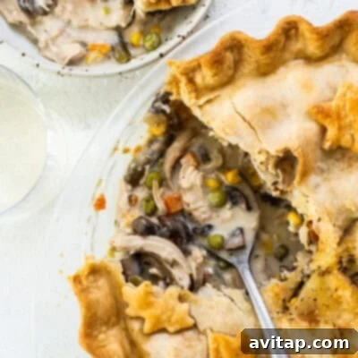 A golden-brown chicken pot pie on a plate with a slice removed, revealing the creamy filling.