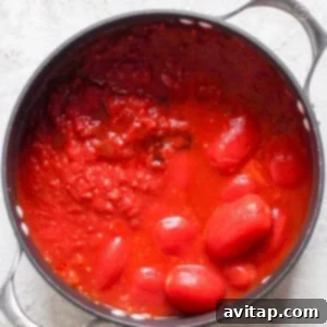 A black pot filled with whole and crushed tomatoes in tomato sauce, reminiscent of a comforting bowl of tomato soup, sits on a light gray surface. Perfect for pairing with a crispy grilled cheese sandwich.
