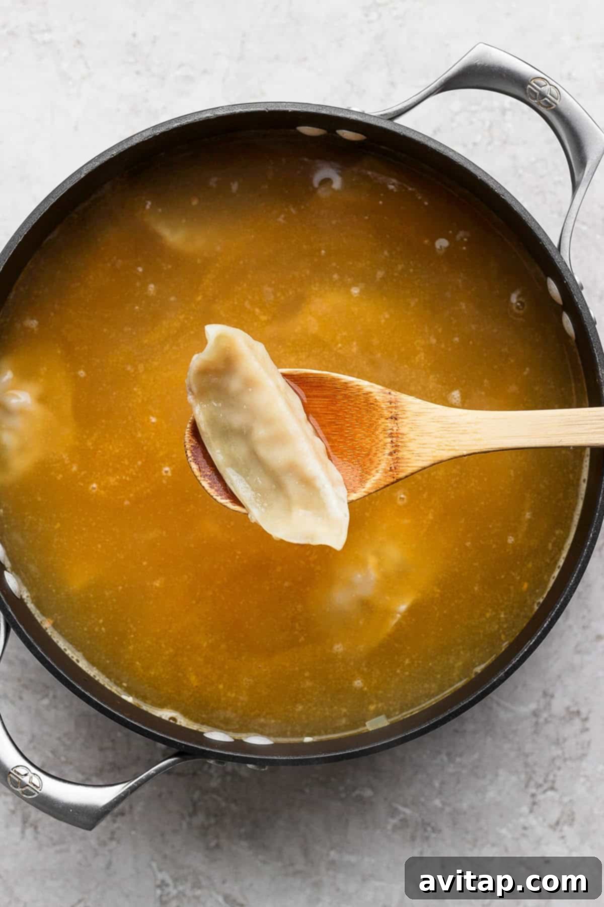 Zesty Wonton Delight 3 A pot of broth with a wooden spoon holding a dumpling above the liquid.