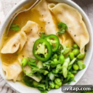 Zesty Wonton Delight 4 A bowl of soup with dumplings, topped with sliced jalapeños, edamame, green onions, and cilantro.