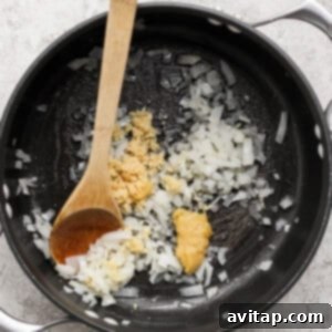 Zesty Wonton Delight 6 Chopped onions and minced garlic sauté in a black pot with a wooden spoon on a gray textured surface.
