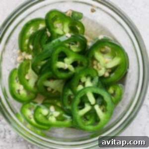 Zesty Wonton Delight 9 A glass bowl filled with sliced green jalapeños on a light gray surface.