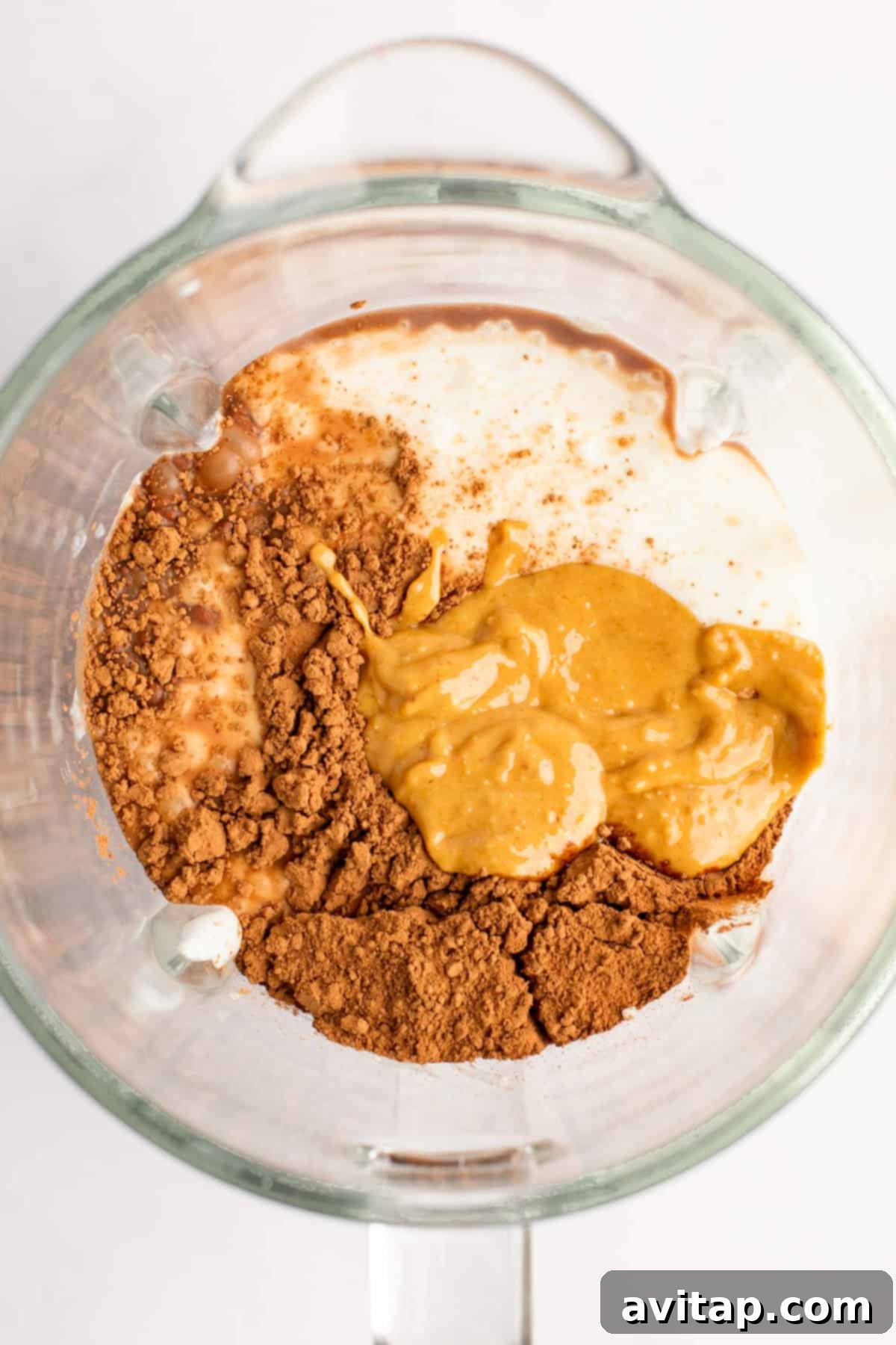 Top view of a blender jar containing cocoa powder, peanut butter, and milk, ready to be blended.