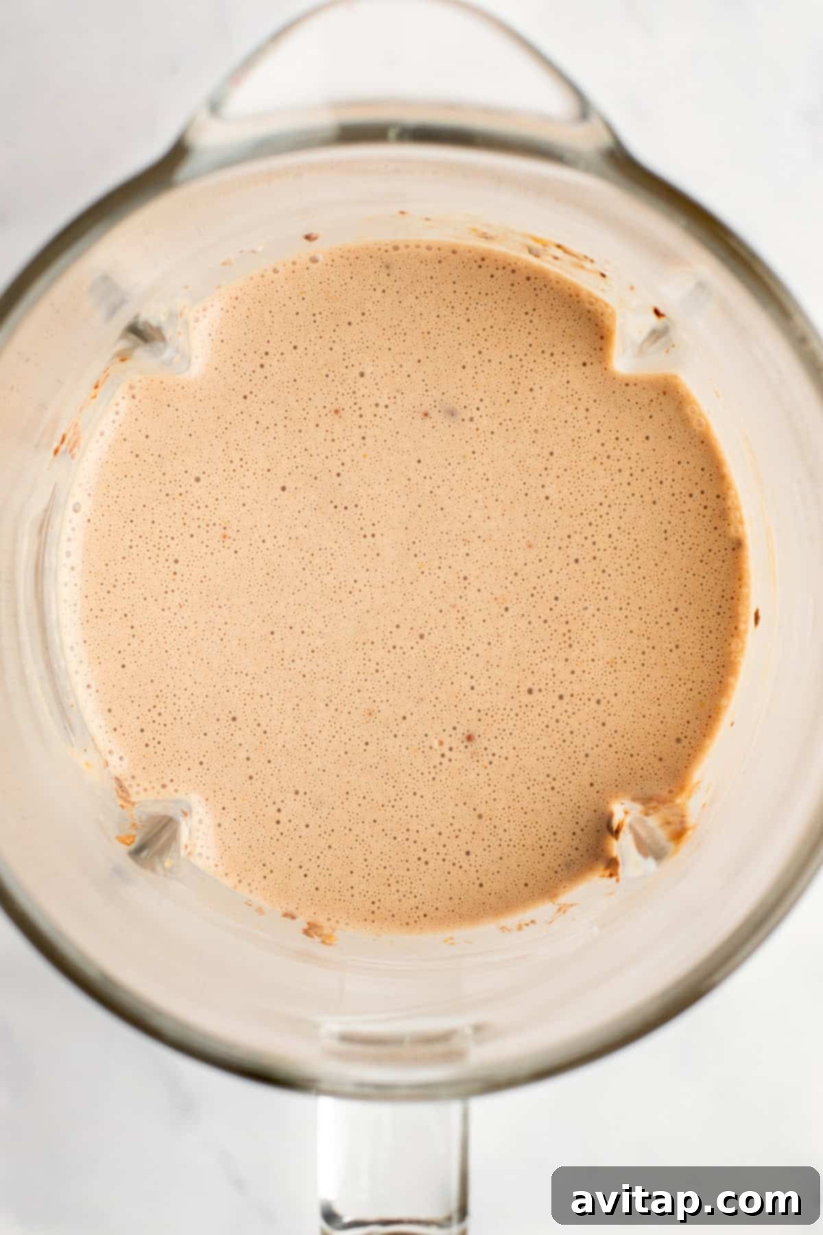 A top view of a blender containing a smooth, light brown liquid mixture.