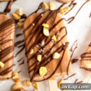Chocolate-coated ice cream bar sprinkled with nuts and drizzled chocolate on parchment paper.