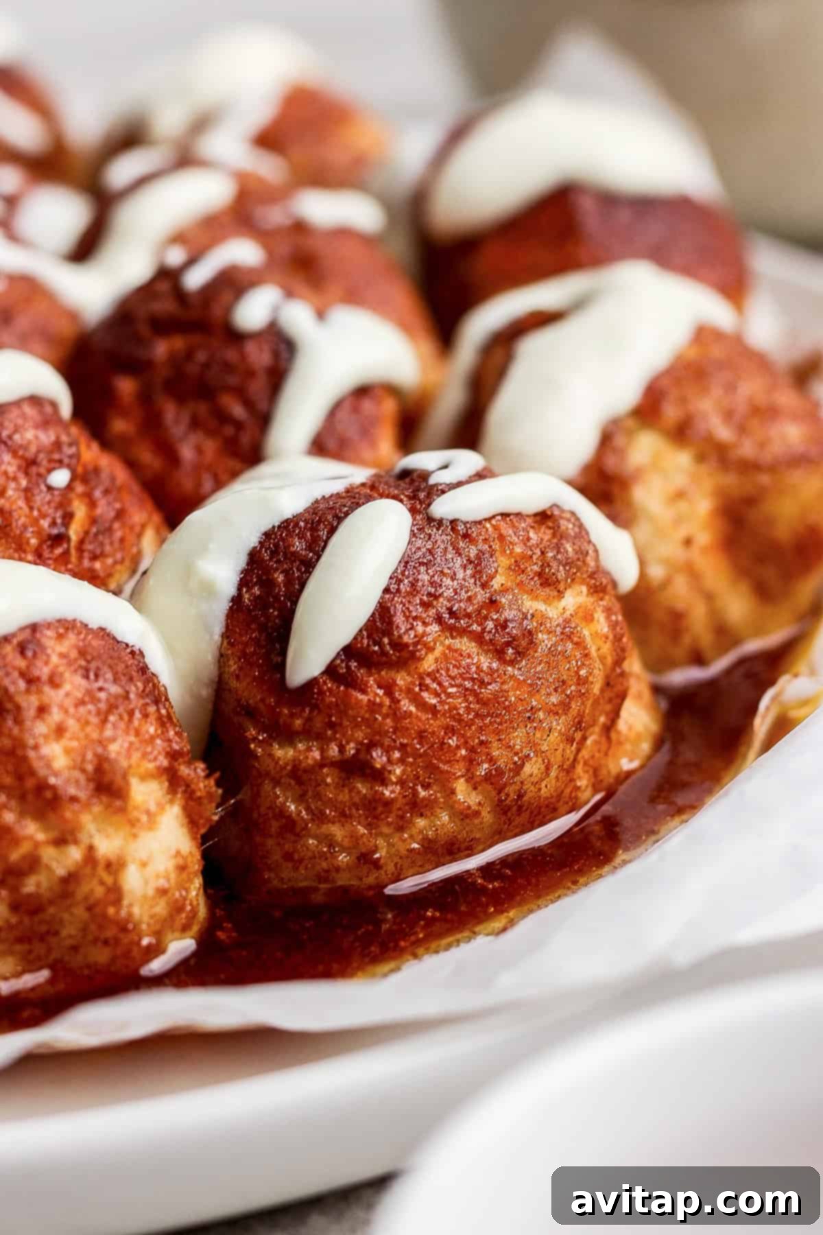 Close-up of cinnamon rolls topped with white icing, arranged on wax paper.