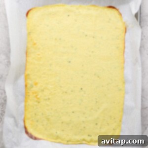 A rectangular sheet of pale yellow flatbread on parchment paper, placed on a baking tray.