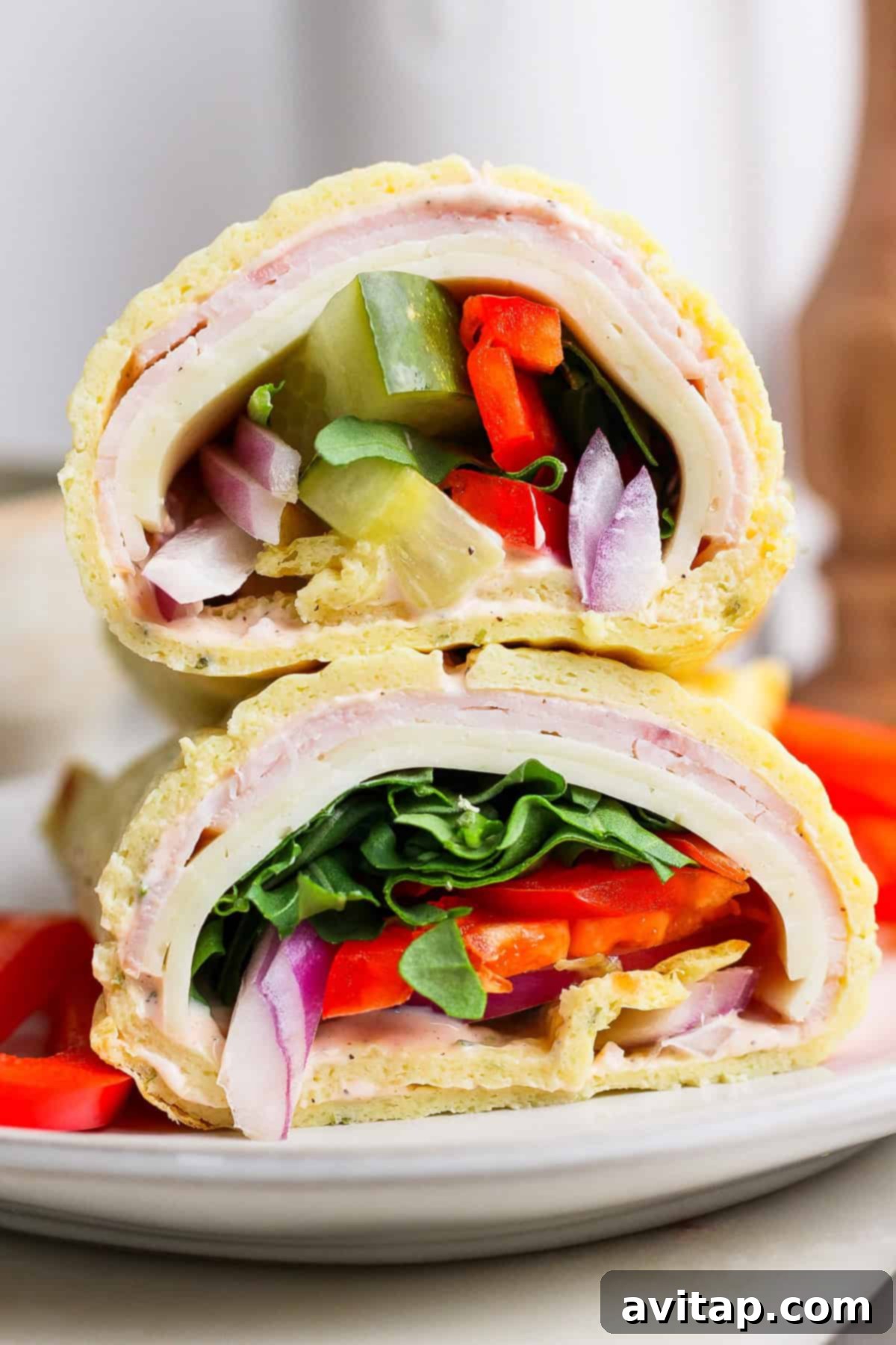 Close-up of two sandwich halves stacked, featuring layers of turkey, cheese, spinach, tomato, onion, and green pepper on a rolled flatbread. Resembling cottage cheese wraps in their wholesome appeal, they rest invitingly on a white plate.