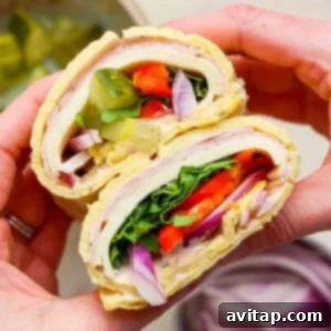 Hands holding a delicious cottage cheese wrap filled with turkey, lettuce, tomato, pickles, red onion, and spinach.