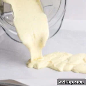 Thick yellow batter is being poured from a blender onto a lined baking sheet.
