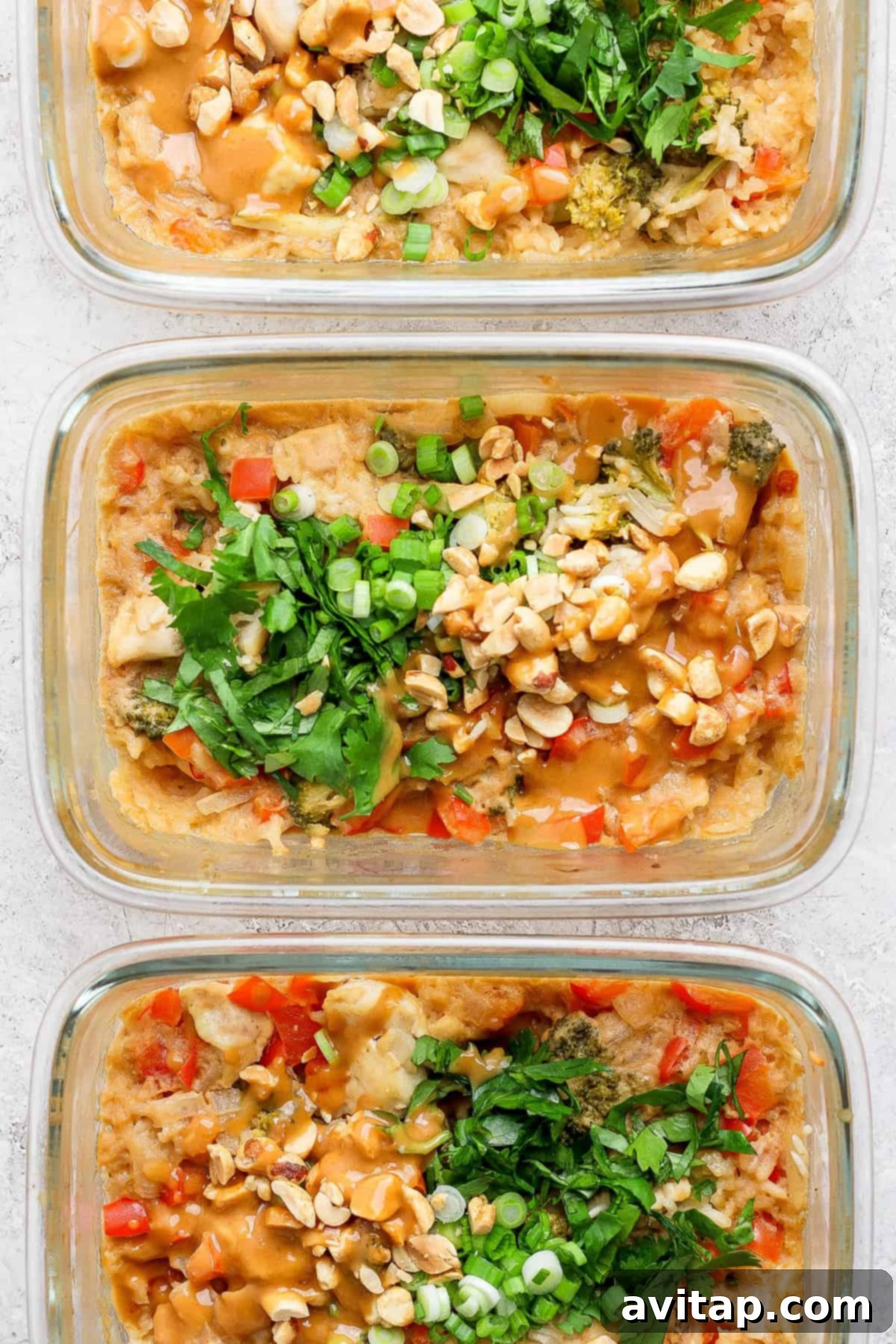 Three glass containers filled with a delicious dish featuring rice, diced vegetables, chopped nuts, and tender peanut chicken, all garnished with fresh herbs and green onions.