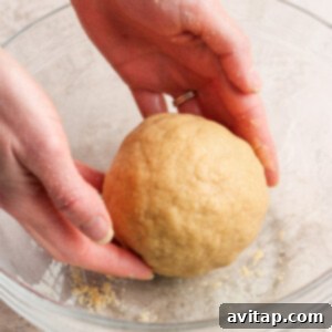 Hands shaping a ball of dough in a clear glass bowl on a light-colored surface.