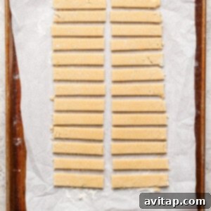 Strips of dough neatly arranged on a parchment-lined baking sheet.
