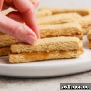A hand picks up a peanut butter sandwich cookie from a white plate. More cookies are visible in the background.