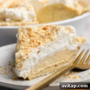 Wholesome Protein Pie Crust 3 A perfectly sliced piece of protein coconut cream pie on a white plate with a golden fork, elegantly topped with fluffy whipped cream and golden toasted coconut flakes.