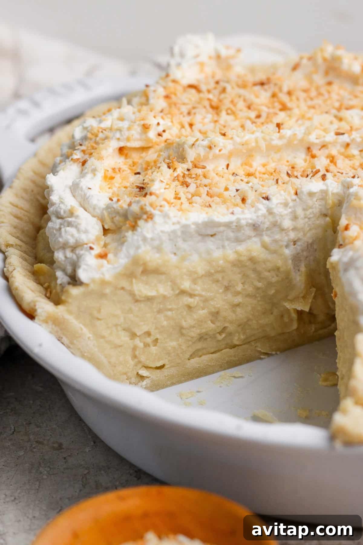 Wholesome Protein Pie Crust 6 A perfectly baked protein coconut cream pie with a delicious slice carefully removed, revealing the creamy filling and the golden, flaky crust. The pie is beautifully adorned with fluffy whipped cream and golden toasted coconut flakes, presented in a classic white ceramic pie dish.