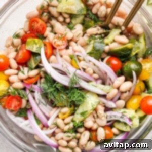 Bowl of white bean salad with cherry tomatoes, cucumber, red onion, and dill.