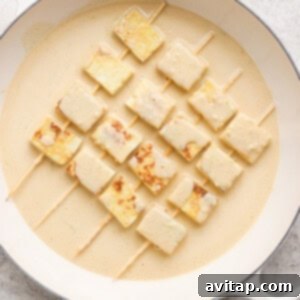 Skewered tofu cubes in creamy marinade on a round white dish.