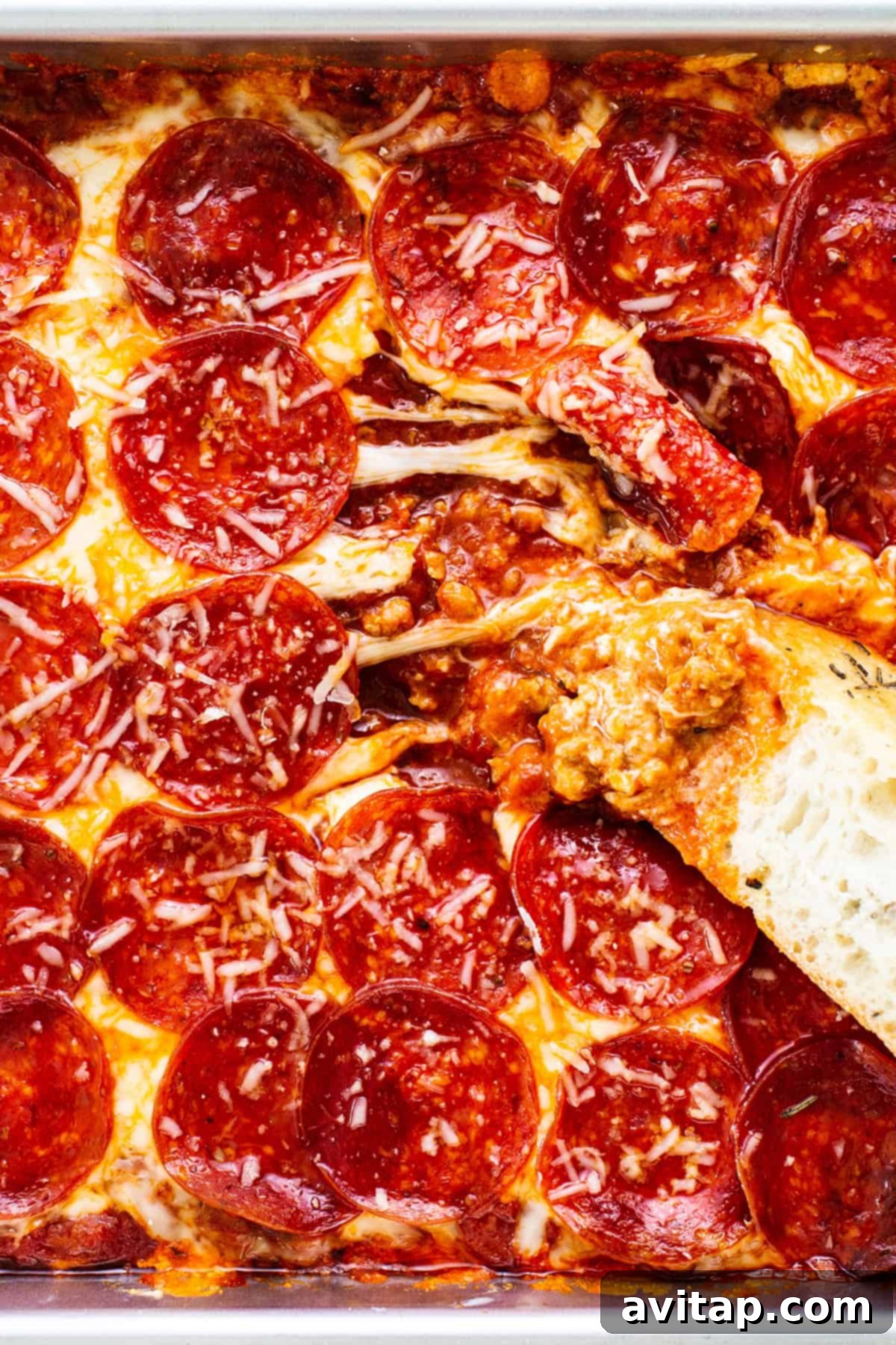 Close-up of a pepperoni pizza dip with melted cheese, pepperoni slices, and a piece of bread dipped into the mixture.