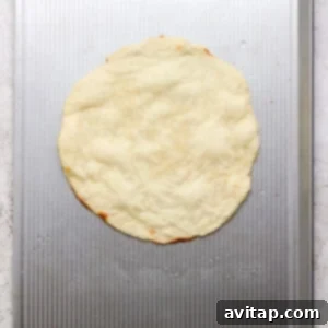 A round, uncooked pizza dough is placed on a metal baking sheet with a textured surface.