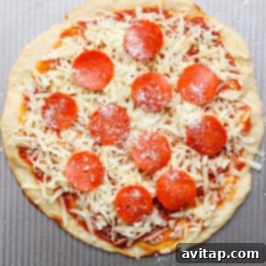 Unbaked pizza with pepperoni slices, grated cheese, and sauce on a round dough placed on a textured metal surface.