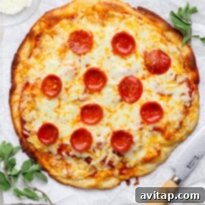 A pepperoni pizza on parchment paper with a knife beside it, garnished with herbs. A small bowl of grated cheese is in the top-left corner.