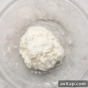 A ball of dough in a clear glass bowl on a light textured surface.