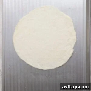 A round, uncooked pizza dough is placed on a textured metal baking sheet.