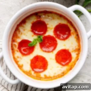 Baked dish with melted cheese and six pepperoni slices, garnished with basil, in a white ceramic bowl on a textured surface, showcasing the delicious final product.