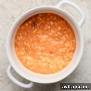 A white ceramic bowl filled with creamy tomato soup, representing the cottage cheese, pizza sauce, and Italian seasoning mixture, placed on a textured light gray surface.